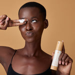 Woman holding the Morning Brightness moisturizer bottle while a small amount of cream is on her finger over her eye.
